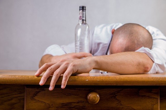 A man slumped at a bar hungover with a bottle of alcohol