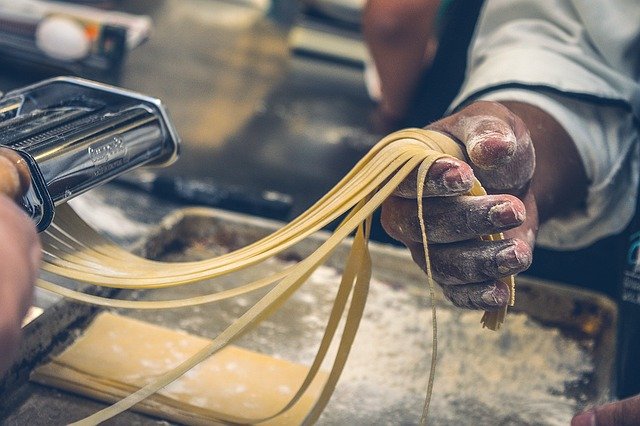 A man holding strings of fresh pasta.